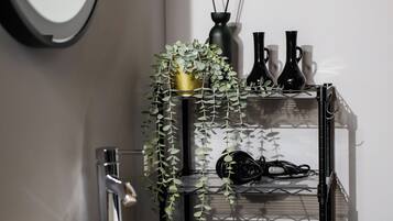 Et badeværelse med en hvid vask, et spejl, en sort hylde med pynteting og en træbordplade.