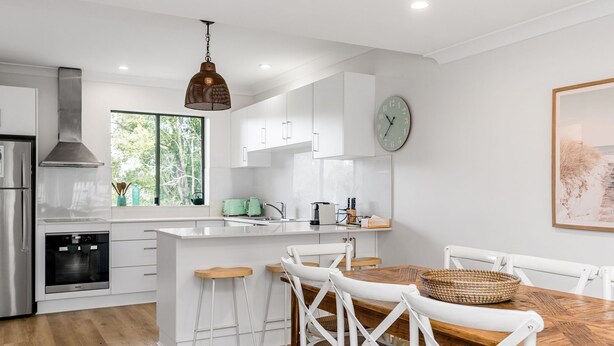 Une cuisine moderne avec des meubles blancs, une table à manger en bois et un luminaire suspendu.