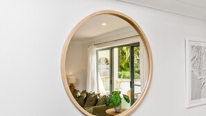 Un miroir rond reflétant un salon avec un canapé, des coussins, une lampe et une plante en pot.