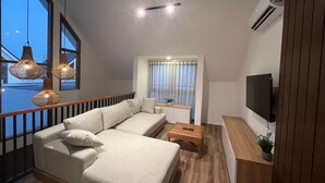 Ein modernes Wohnzimmer mit Sofa, Couchtisch und Fernseher. Hängelampen und ein Fenster mit Vorhängen.