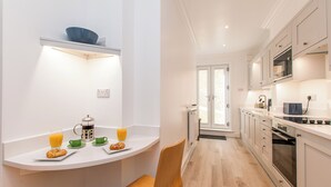 A modern kitchen with white cabinetry, a breakfast setup on a white countertop, and a view into the dining area.