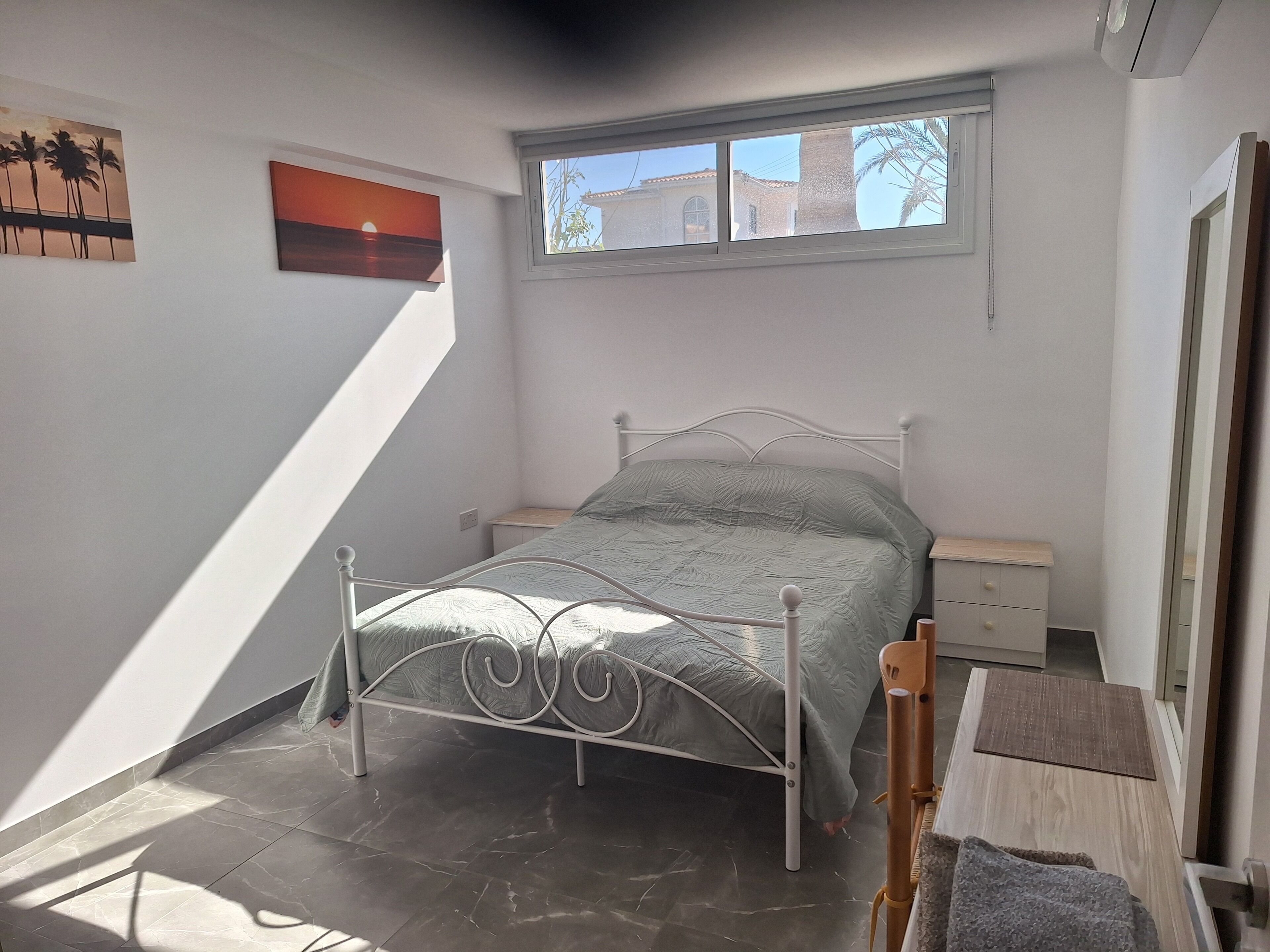 Ein Schlafzimmer mit Bett, Nachttisch, Kommode, Fenster und einem Bild an der Wand.