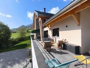 En balkon med udendørs møbler, en stenvæg og udsigt over en grøn dal.