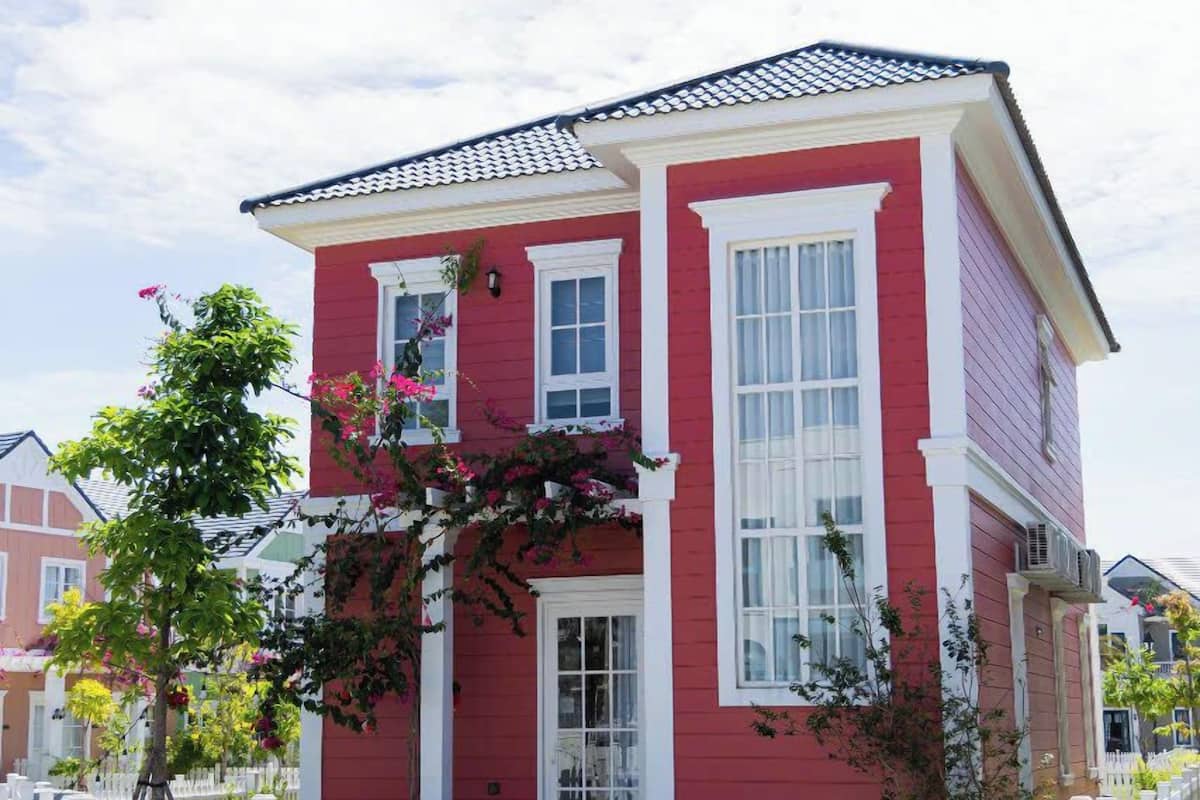 Een tweelaags rood huis met witte details, een wit hek en een kleine boom met roze bloemen.
