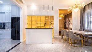 A modern kitchen with white cabinetry, a central island, and a dining area with a chandelier. - Villa LFP Novaworld Phan Thiet (Tien Thanh)
