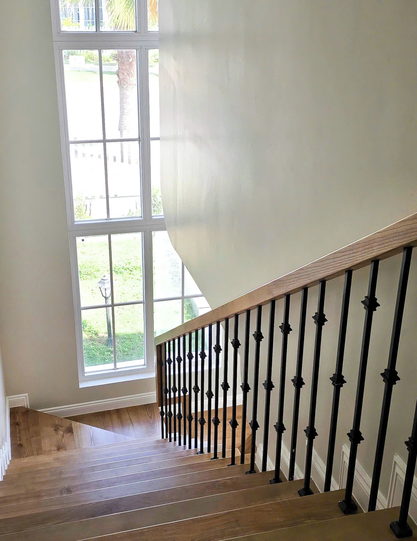 Eine Treppe mit Holzboden und schwarzen Spindeln, die zu einem Zwischenpodest mit großen Fenstern führt, welche einen Blick auf einen Garten bieten.