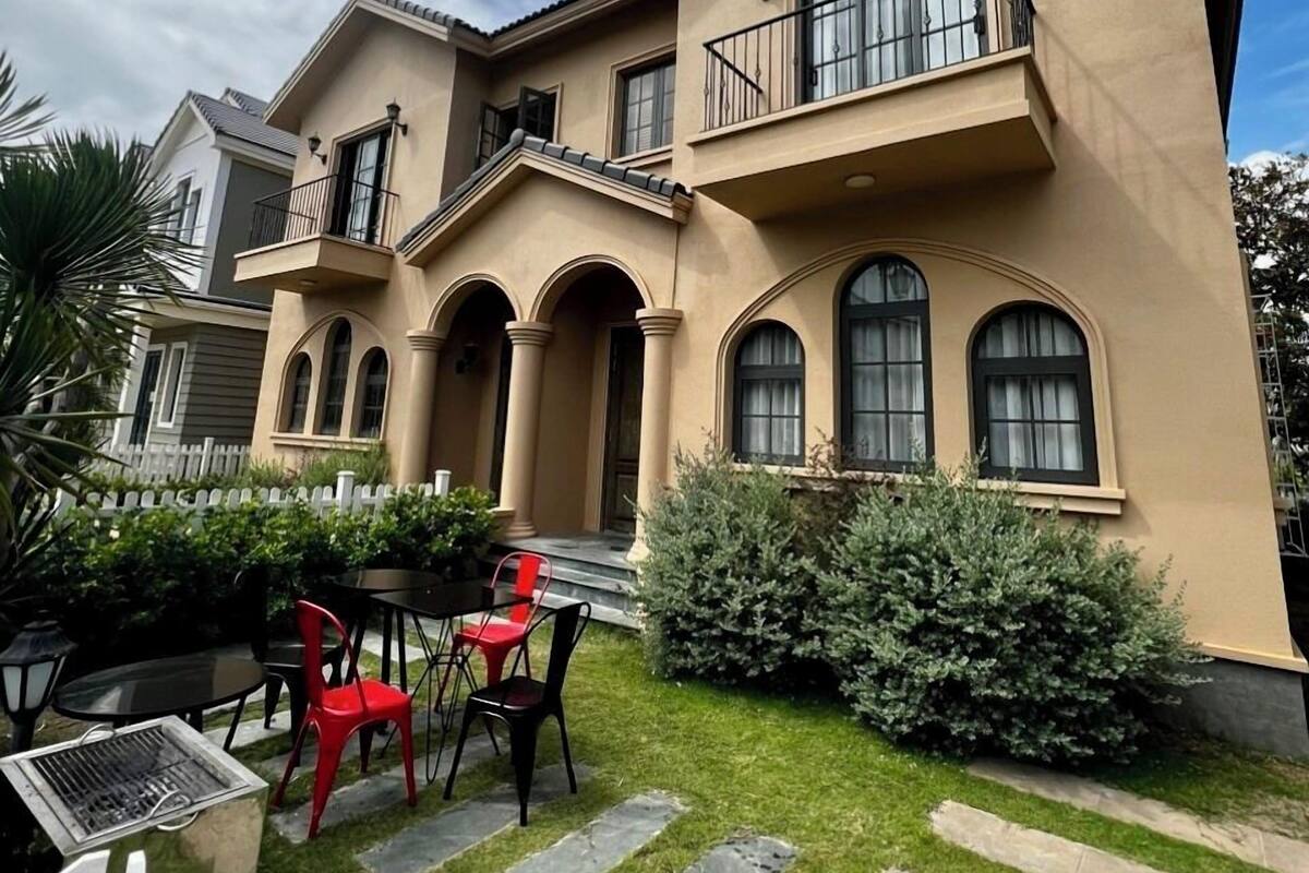 Een tweelaags huis met een balkon, een terras met stoelen en een verzorgd gazon.