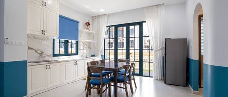 Una cocina moderna con armarios blancos, encimera de mármol y un comedor con sillas tapizadas en azul.