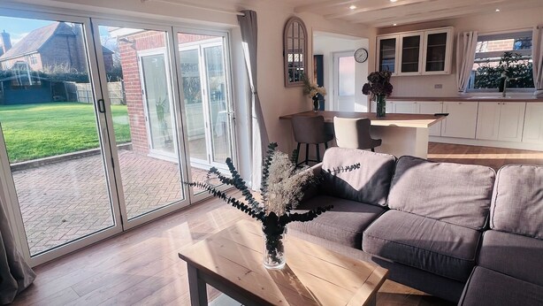 Een moderne woonkamer met een bank, een houten salontafel en uitzicht op een tuin door grote schuifdeuren.