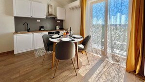 Una cocina moderna con armarios blancos, un comedor con una mesa para dos, y un amplio ventanal con cortinas.