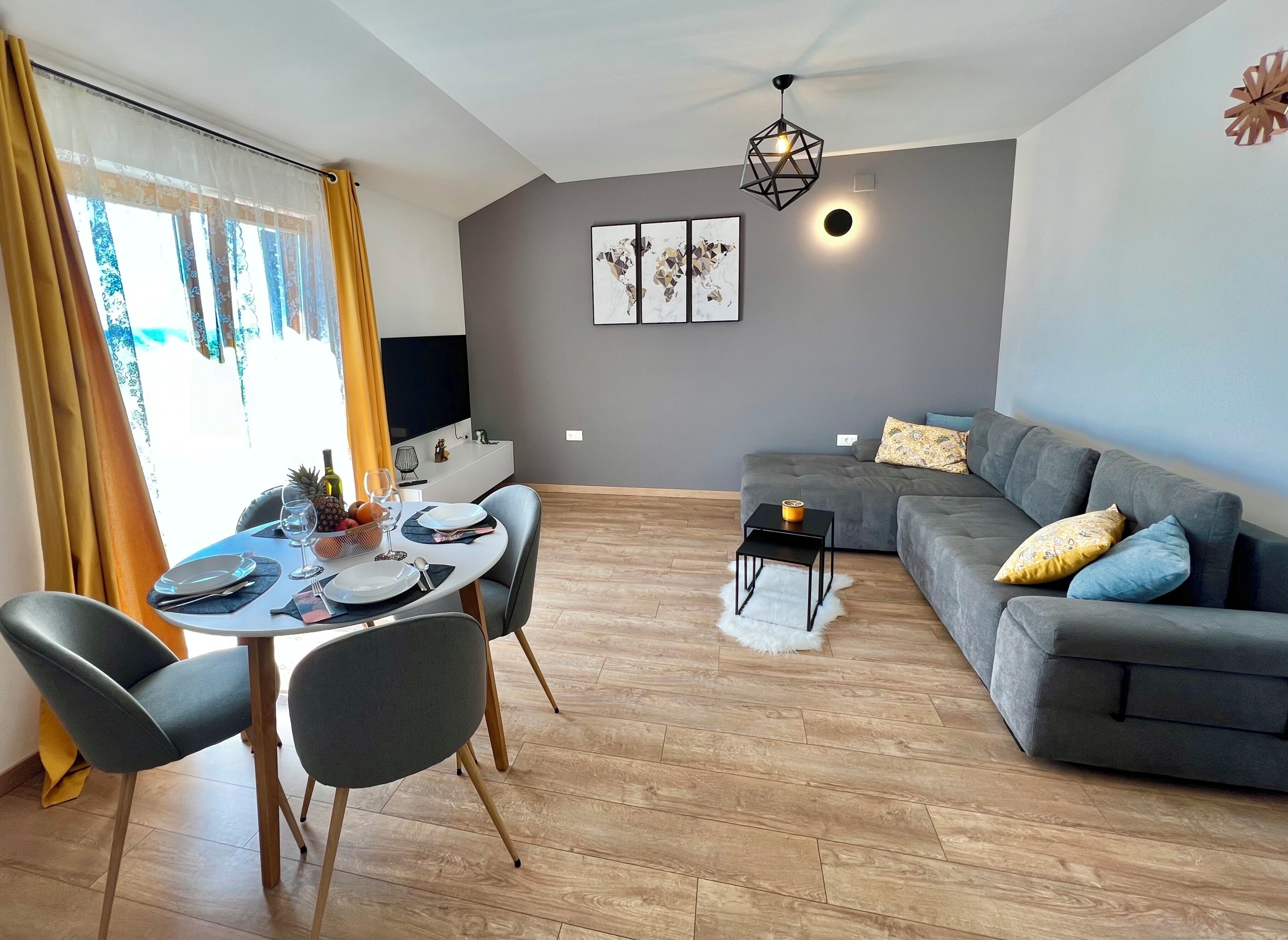 A modern living room with a dining area, grey sofa, and wooden flooring.