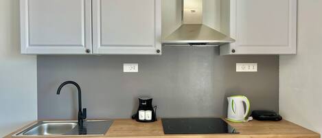 A modern kitchen with white cabinets, a stainless steel sink, a black induction cooktop, a built-in oven, and a kettle.
