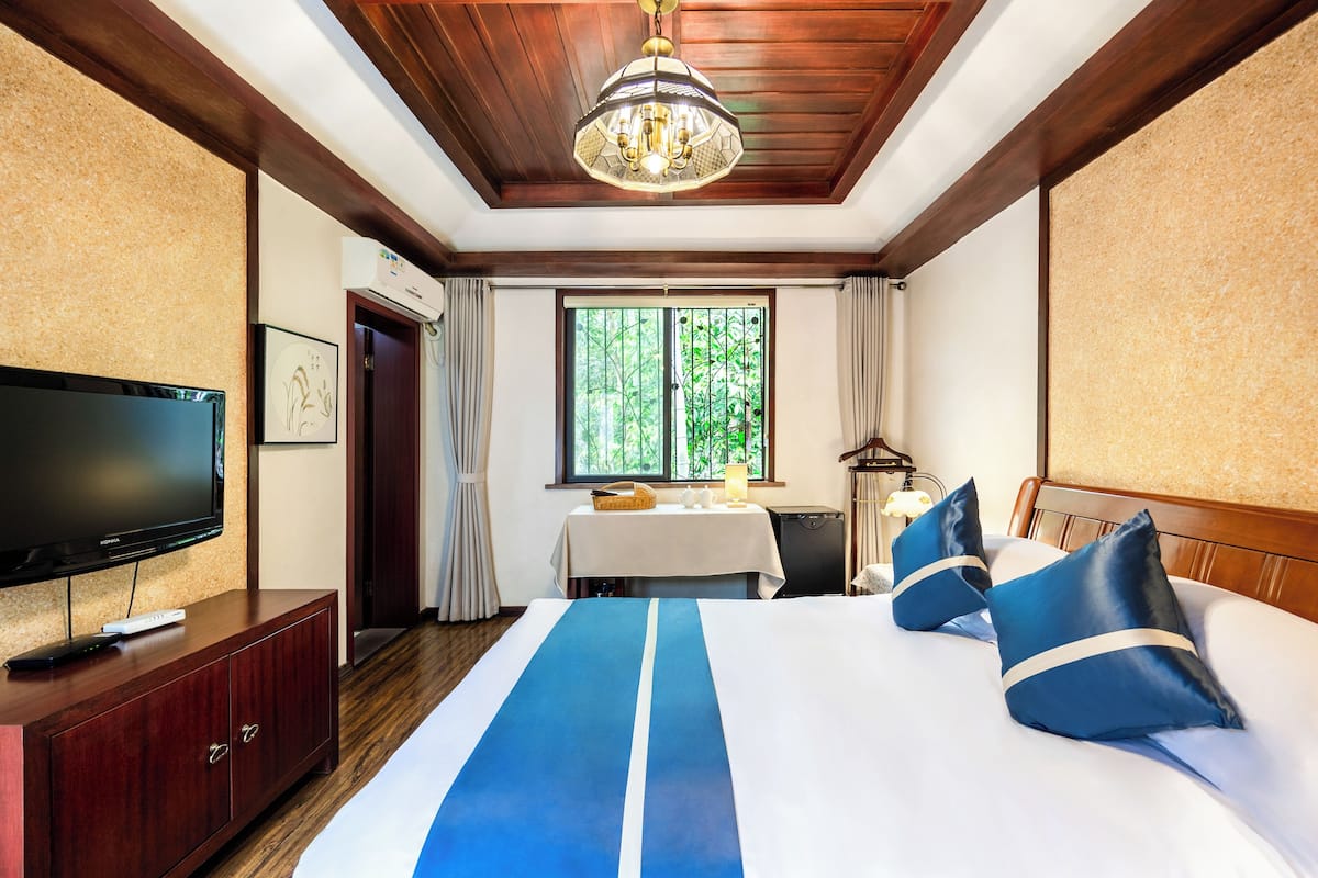 Une chambre d’hôtel avec un grand lit, un téléviseur à écran plat, une tête de lit en bois et une fenêtre donnant sur des arbres.