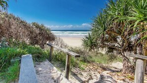 Un sentier en bois menant à une plage offrant une vue sur l’océan, le tout entouré de végétation.