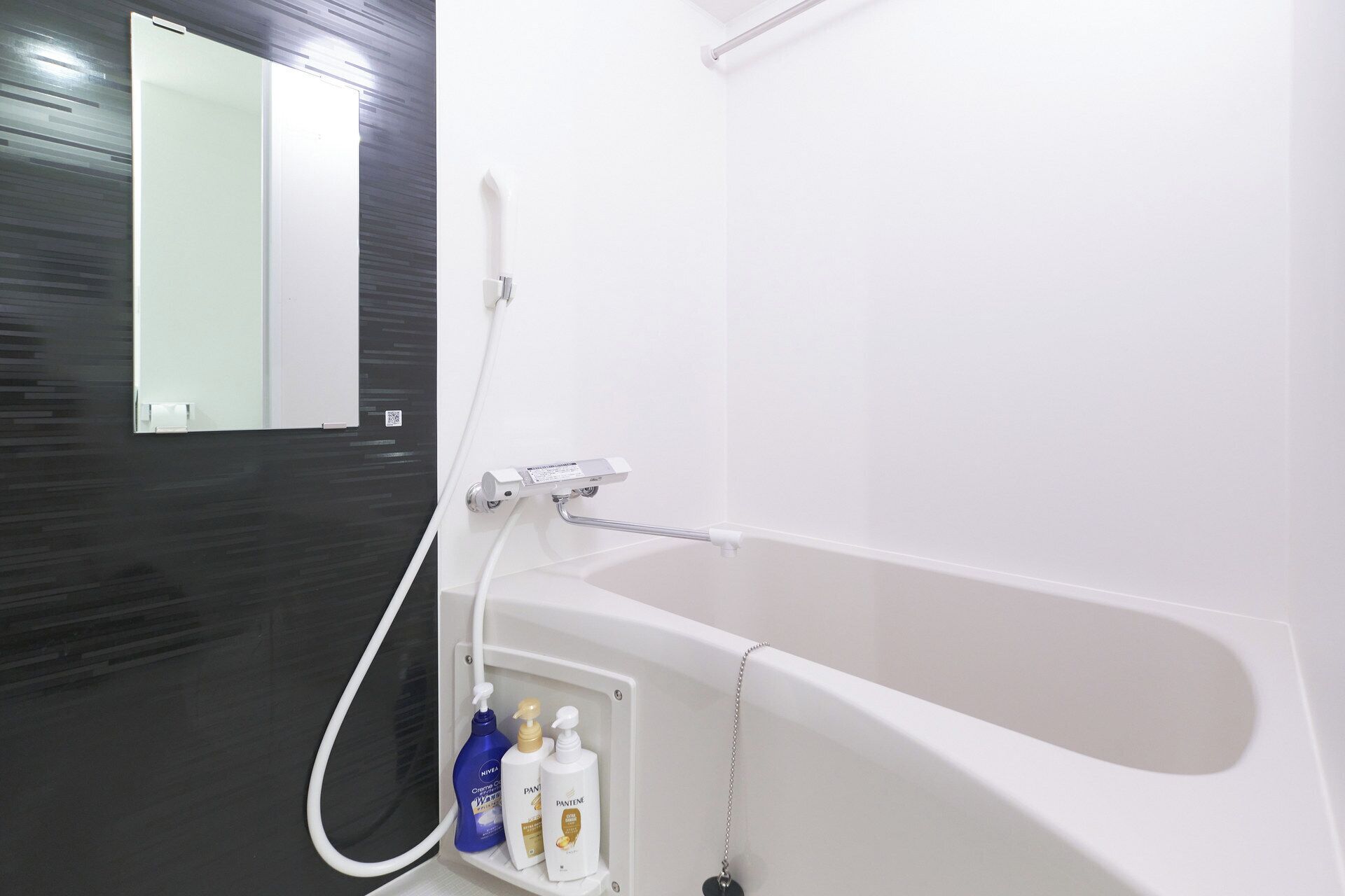 A modern bathroom with a white bathtub, a handheld showerhead, and a mirror.