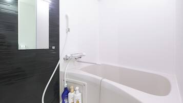 A modern bathroom with a white bathtub, a handheld showerhead, and a mirror.