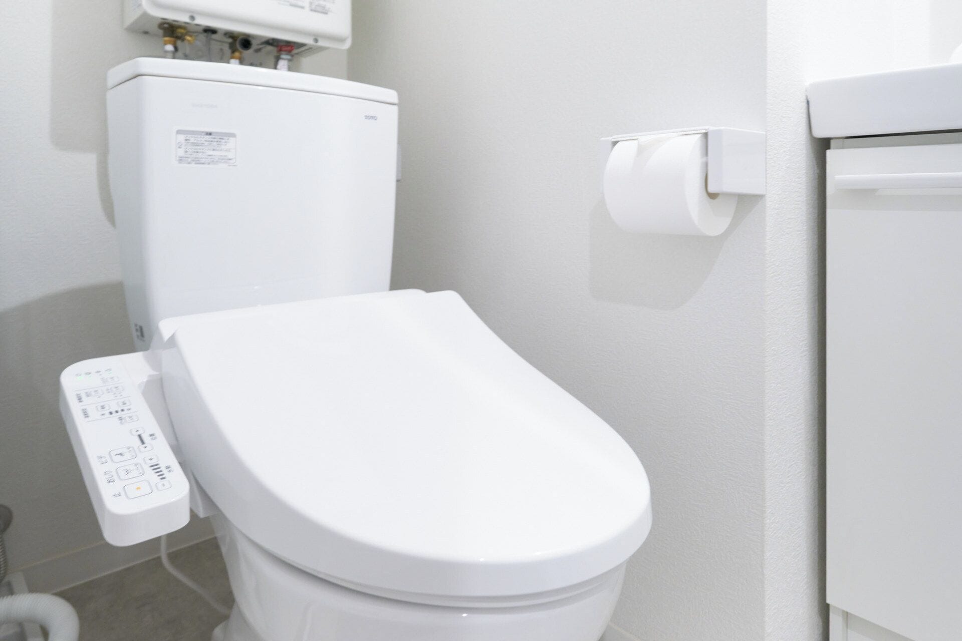 A white toilet with a control panel and a toilet paper holder on the wall.
