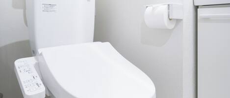 A white toilet with a control panel and a toilet paper holder on the wall.