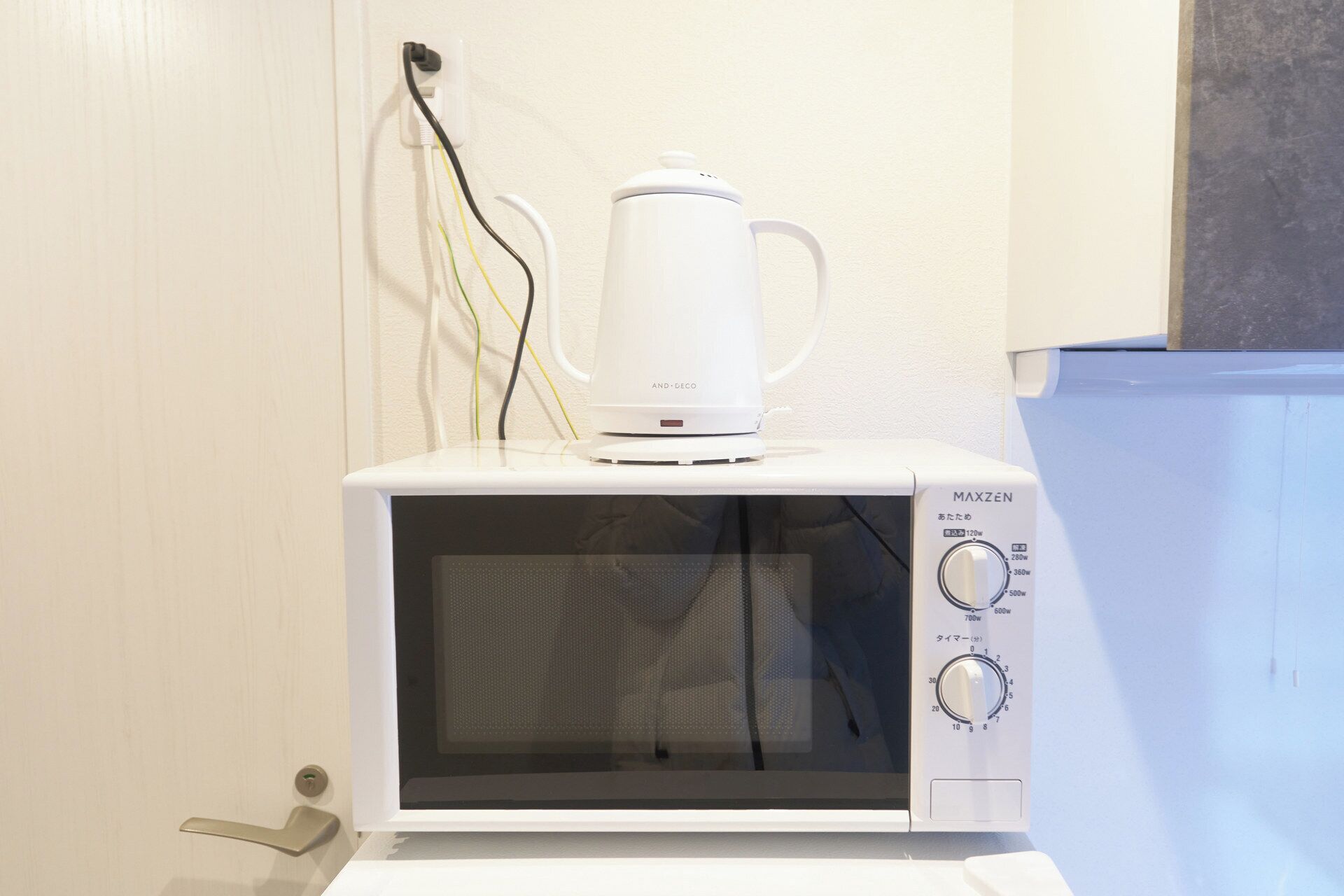 A white microwave oven with a coffee pot on top, connected to a wall outlet with multiple cables.