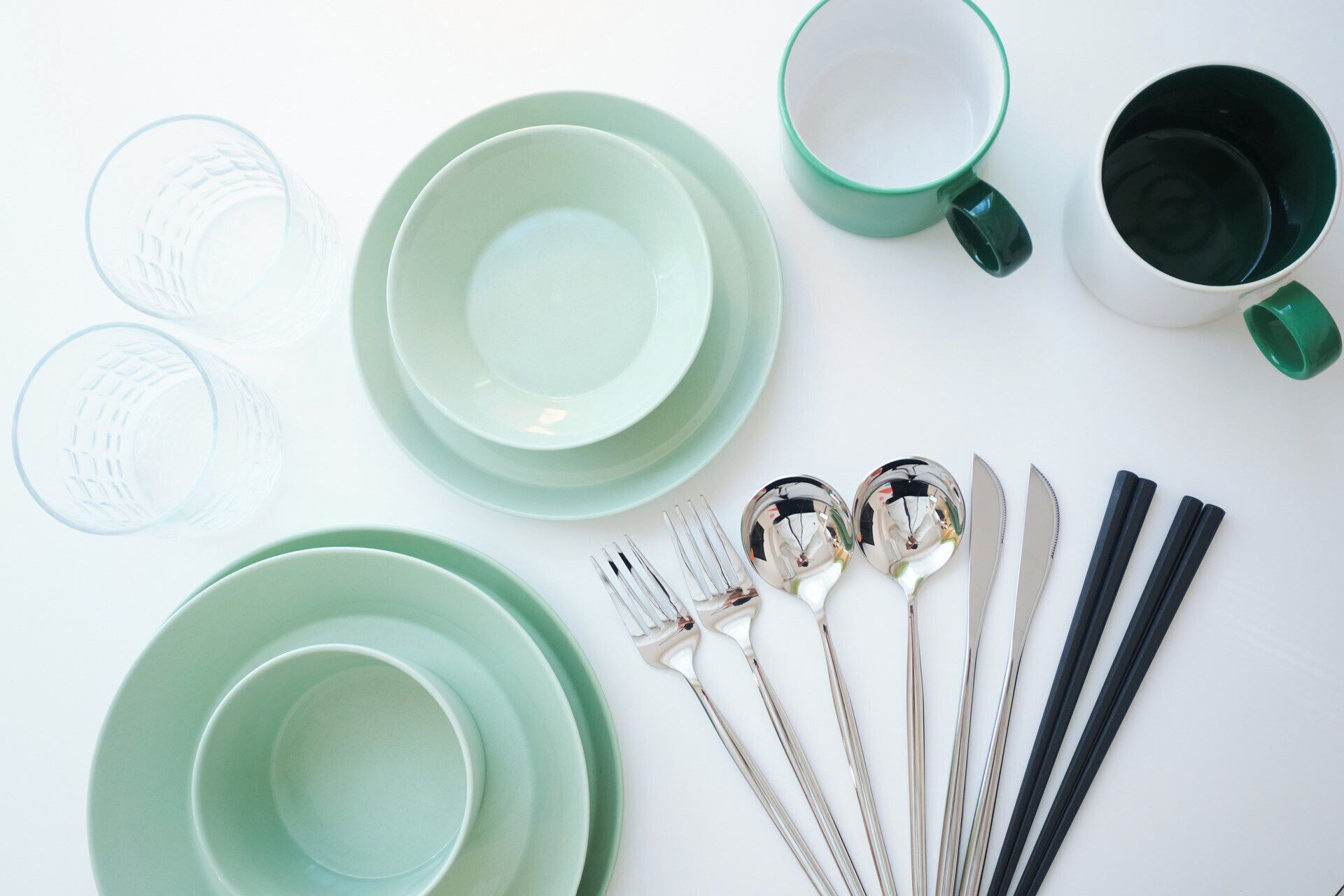 A table set with green plates, cups, and cutlery.