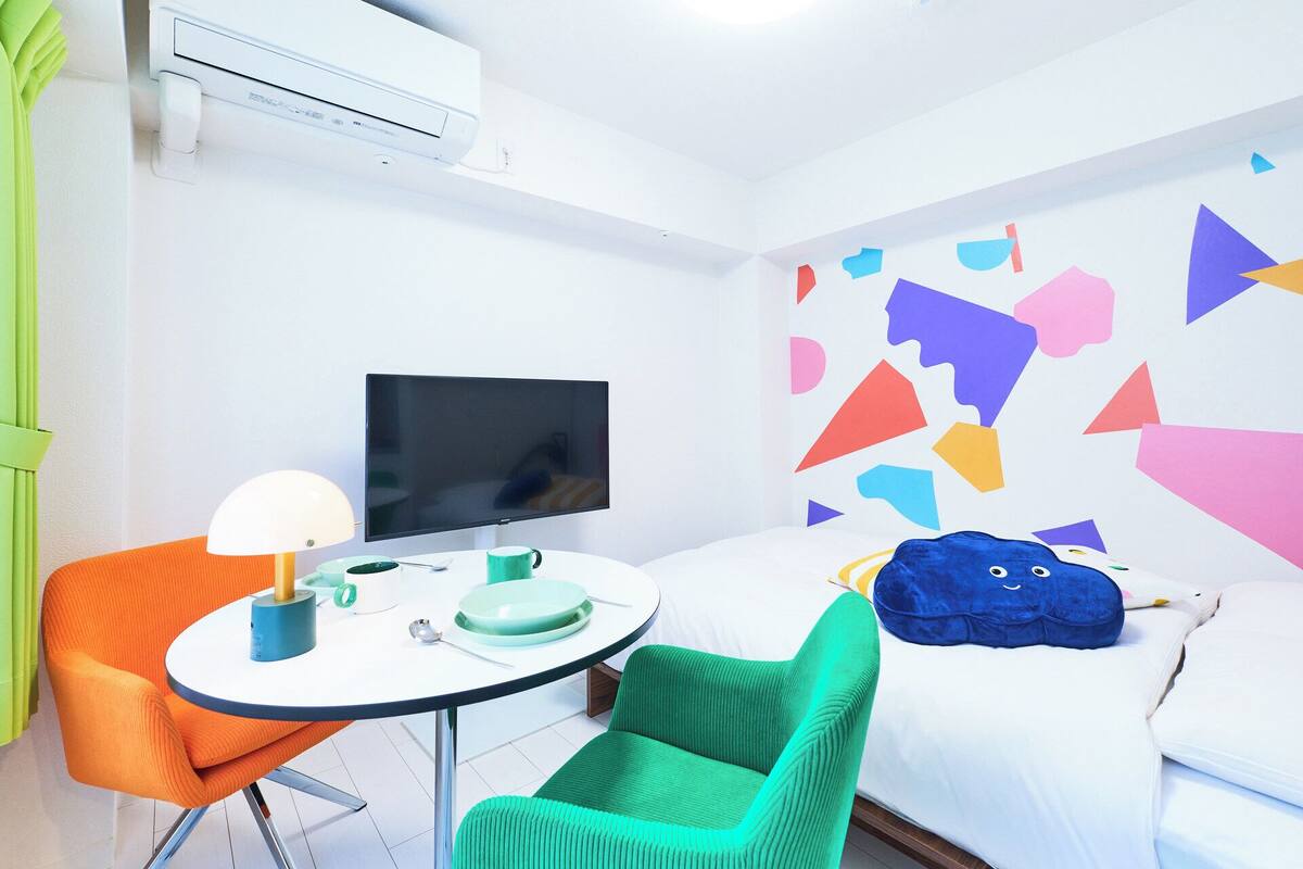 Een hotelkamer met een bed, een televisie, een tafel met stoelen en een kleurrijke wanddecoratie.