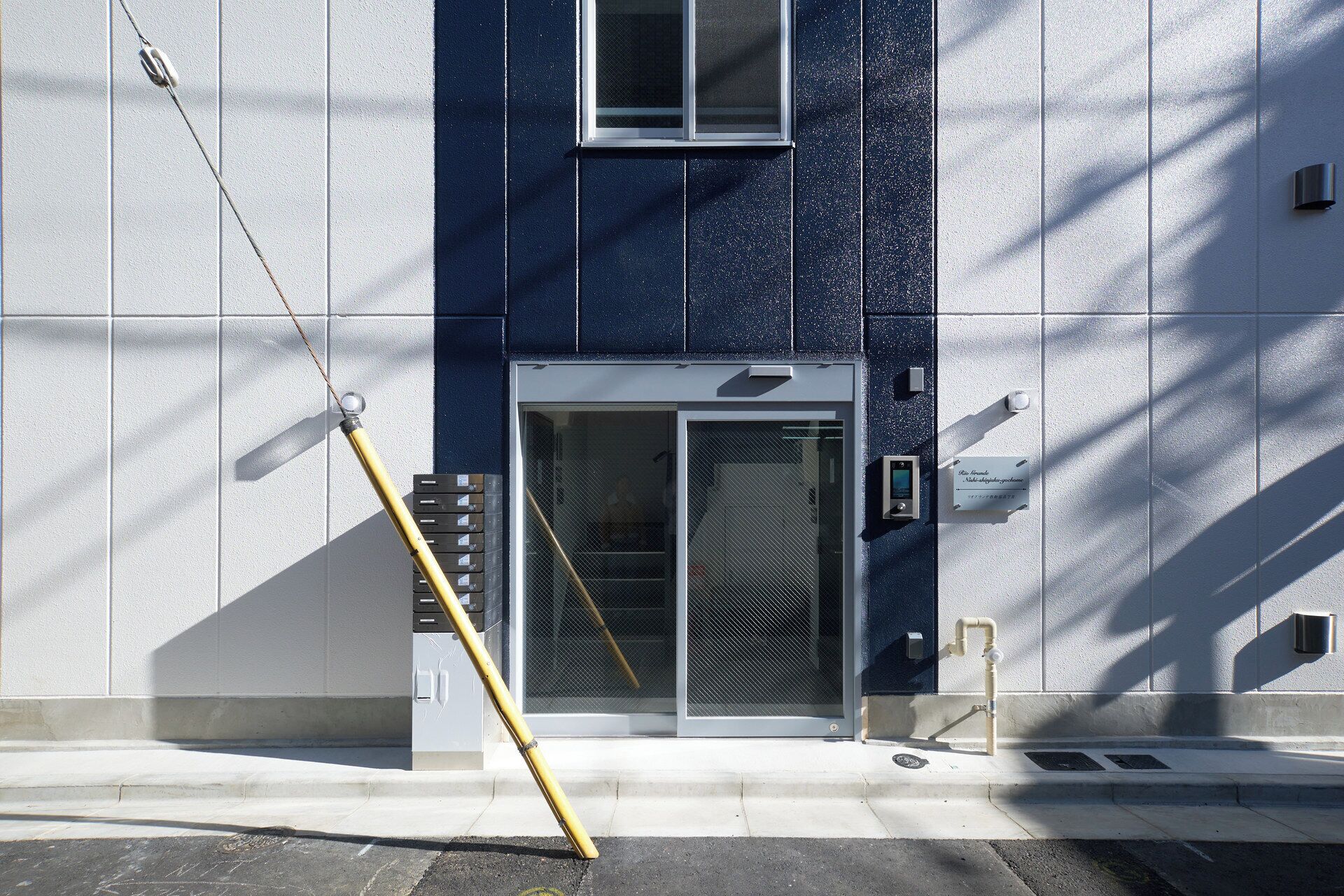 A building facade with a blue and white color scheme, a glass door entrance, and a yellow object leaning against the wall.