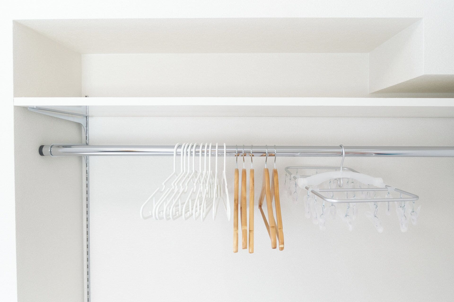 A bathroom with a white shower curtain, a chrome shower rod, and a clear plastic drying rack with wooden-handled hangers.