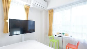 A hotel room with a bed, a flat-screen TV mounted on the wall, a small round table with chairs, and a window with curtains. - Rio Grande Nishi-Shinjuku (Tokyo)