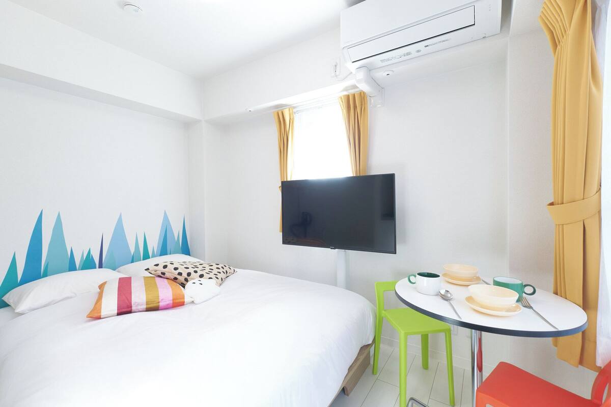 Een hotelkamer met een bed, een flatscreen-tv, een klein tafeltje met een stoel en een raam met gordijnen.