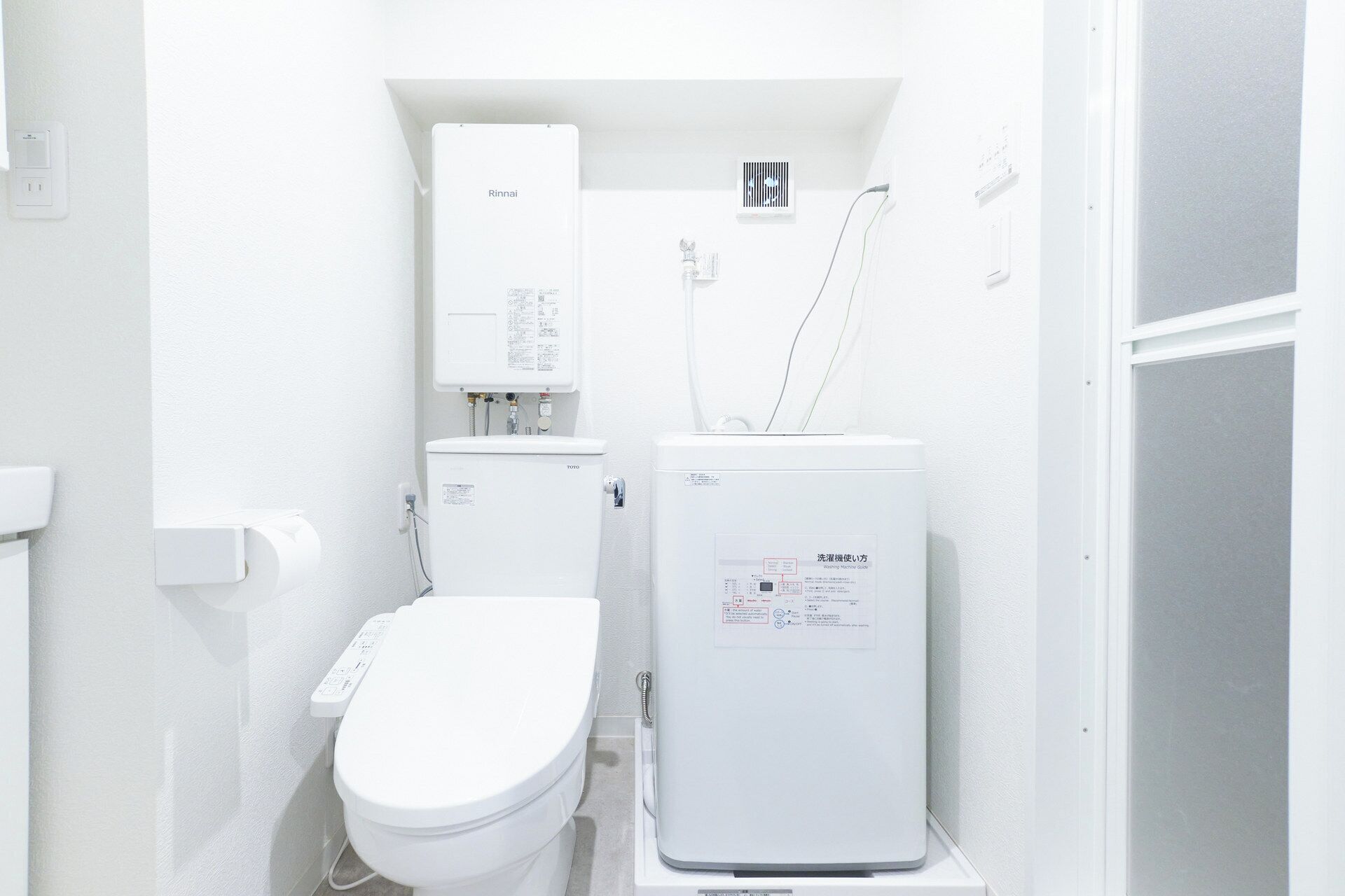 Ein kleines, weißes Badezimmer mit Toilette, Warmwasserbereiter und Bedienfeld.