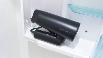 A black hair dryer and a blue container on a white shelf in a bathroom.