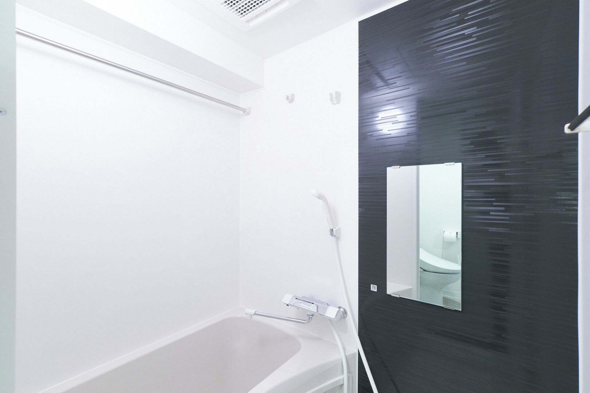 A modern bathroom with a white bathtub, a glass shower enclosure, and a black door with a mirror.