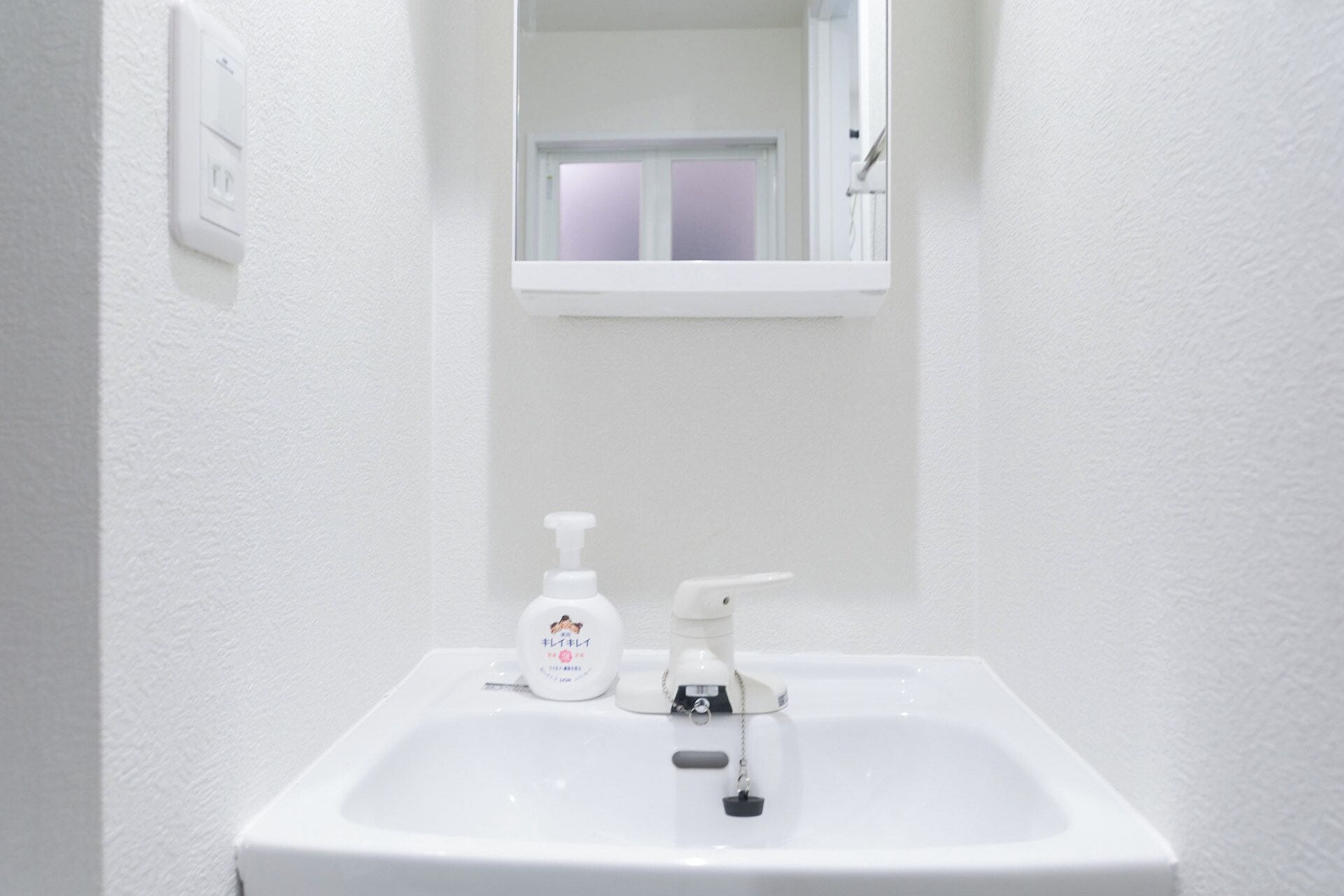 Un lavabo blanc dans une salle de bain, avec un miroir au-dessus, un robinet et un distributeur de savon.