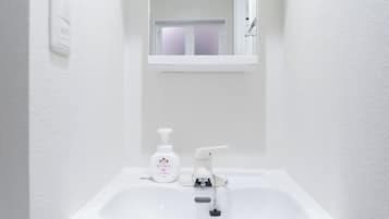 Un lavabo blanc dans une salle de bain, avec un miroir au-dessus, un robinet et un distributeur de savon.