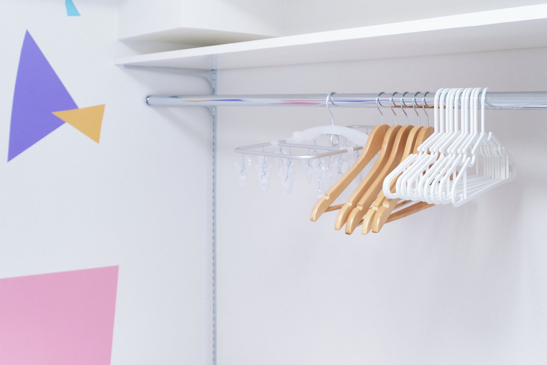 Un portant à vêtements avec des cintres en bois et blancs, dans une pièce dont le mur est blanc et qui est décorée de motifs géométriques.