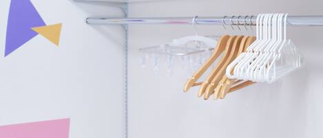 Un portant à vêtements avec des cintres en bois et blancs, dans une pièce dont le mur est blanc et qui est décorée de motifs géométriques.