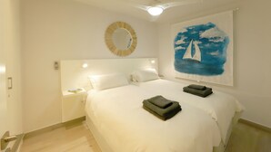 Une chambre d’hôtel avec un grand lit, un ventilateur de plafond, un miroir rond et un tableau représentant un voilier accroché au mur.