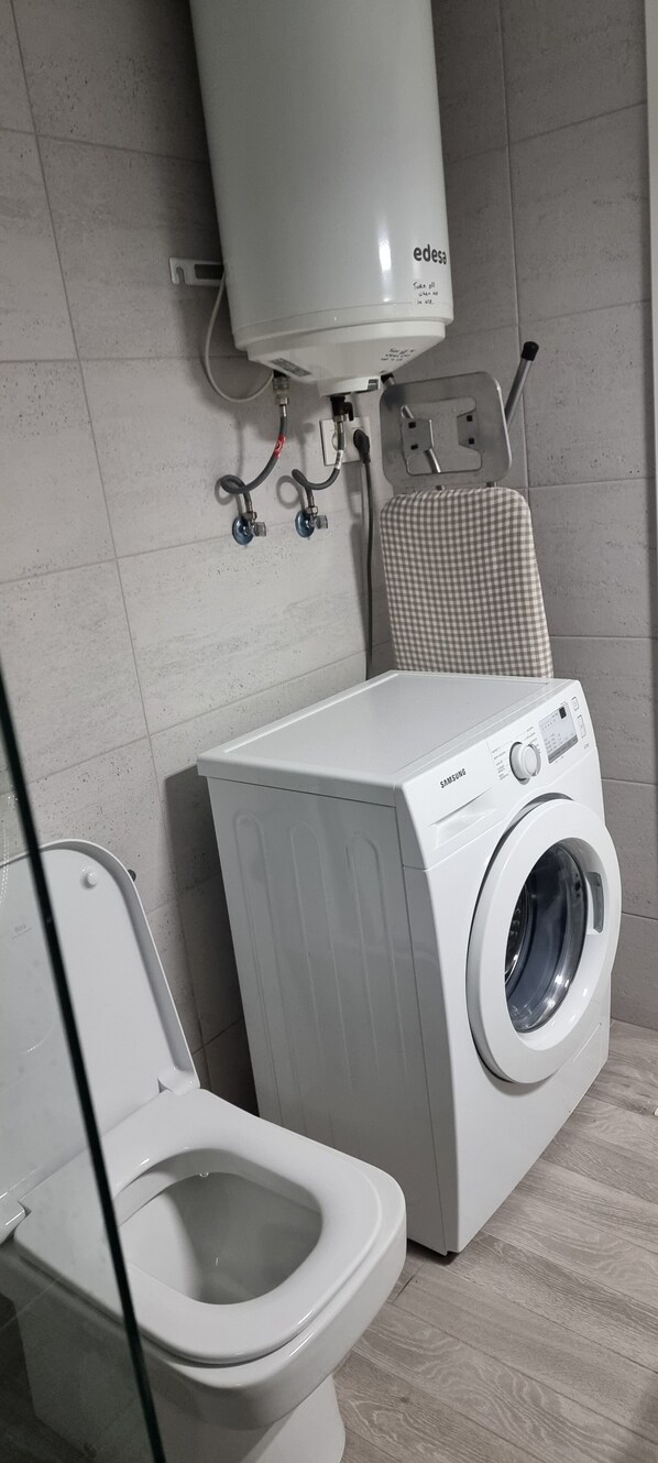 A bathroom with a white toilet, a washing machine, and a water heater.