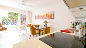Une cuisine moderne avec un îlot central, un coin repas avec des chaises jaunes et une vue sur les palmiers, visible à travers la porte-fenêtre coulissante.