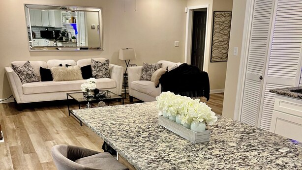 A modern kitchen with a granite countertop, bar stools, and a dining area with a sofa and coffee table. -  Goshen Lake Golf Club Retreat (Augusta)