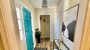 A hallway with a teal door, a black and white patterned rug, a ceiling light fixture, and a wall-mounted shelf with jars. -  Goshen Lake Golf Club Retreat (Augusta)
