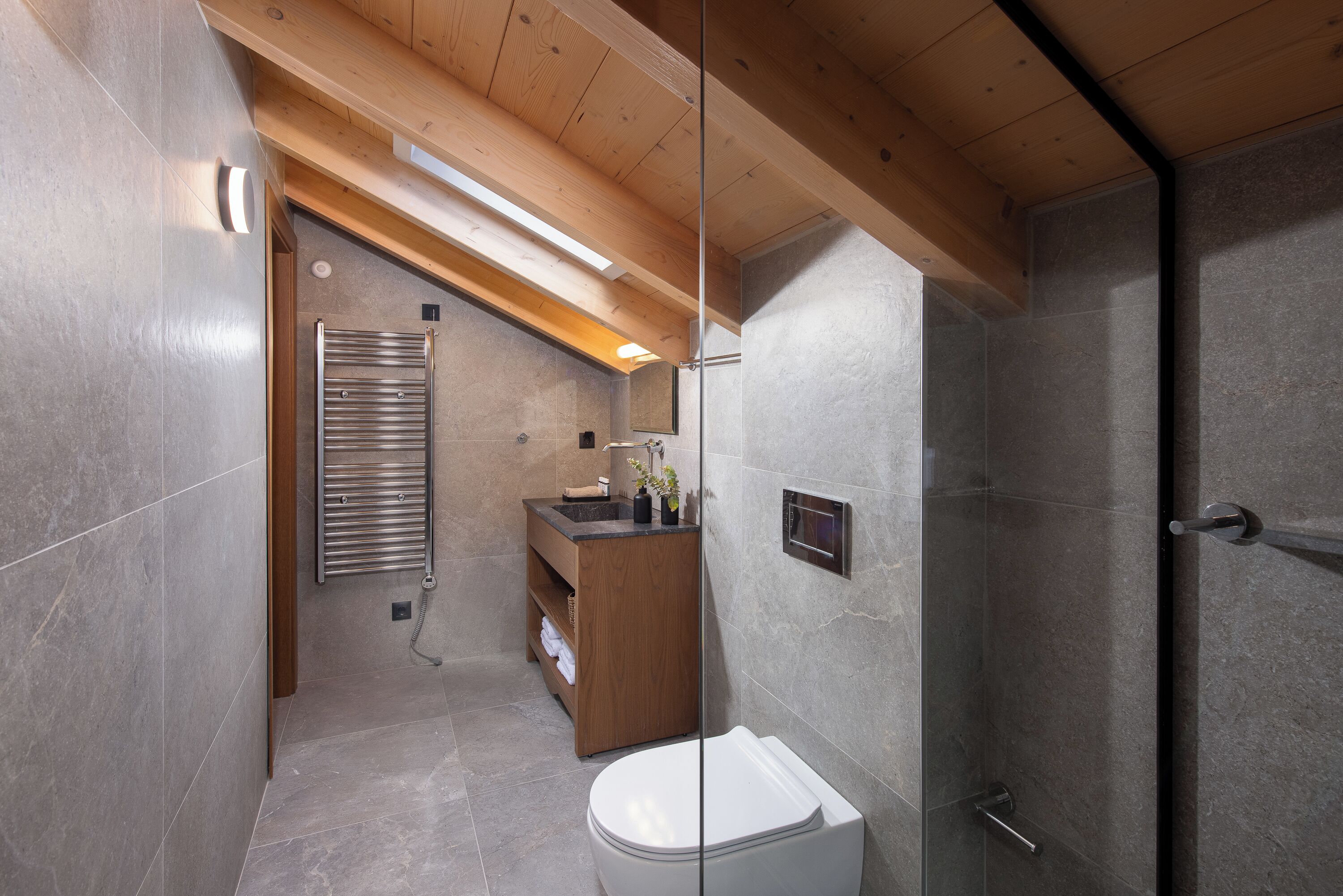 A modern bathroom with a wooden ceiling, a glass shower enclosure, and a built-in sink with a wooden vanity.