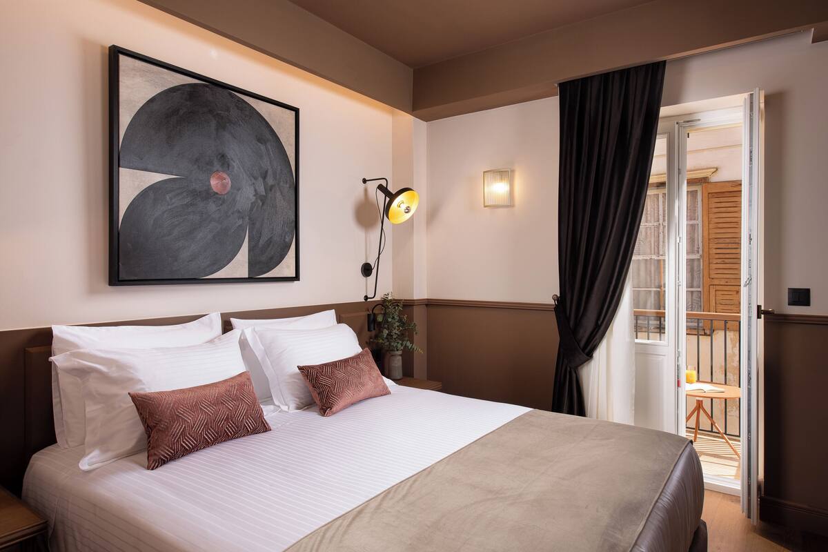 Ett hotellrum med en stor säng, en abstrakt tavla som hänger på väggen, en sänglampa och utsikt över balkongen.
