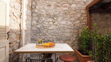 Un muro de piedra, una mesa con fruteros, dos sillas, una pequeña mesa redonda y plantas en macetas.