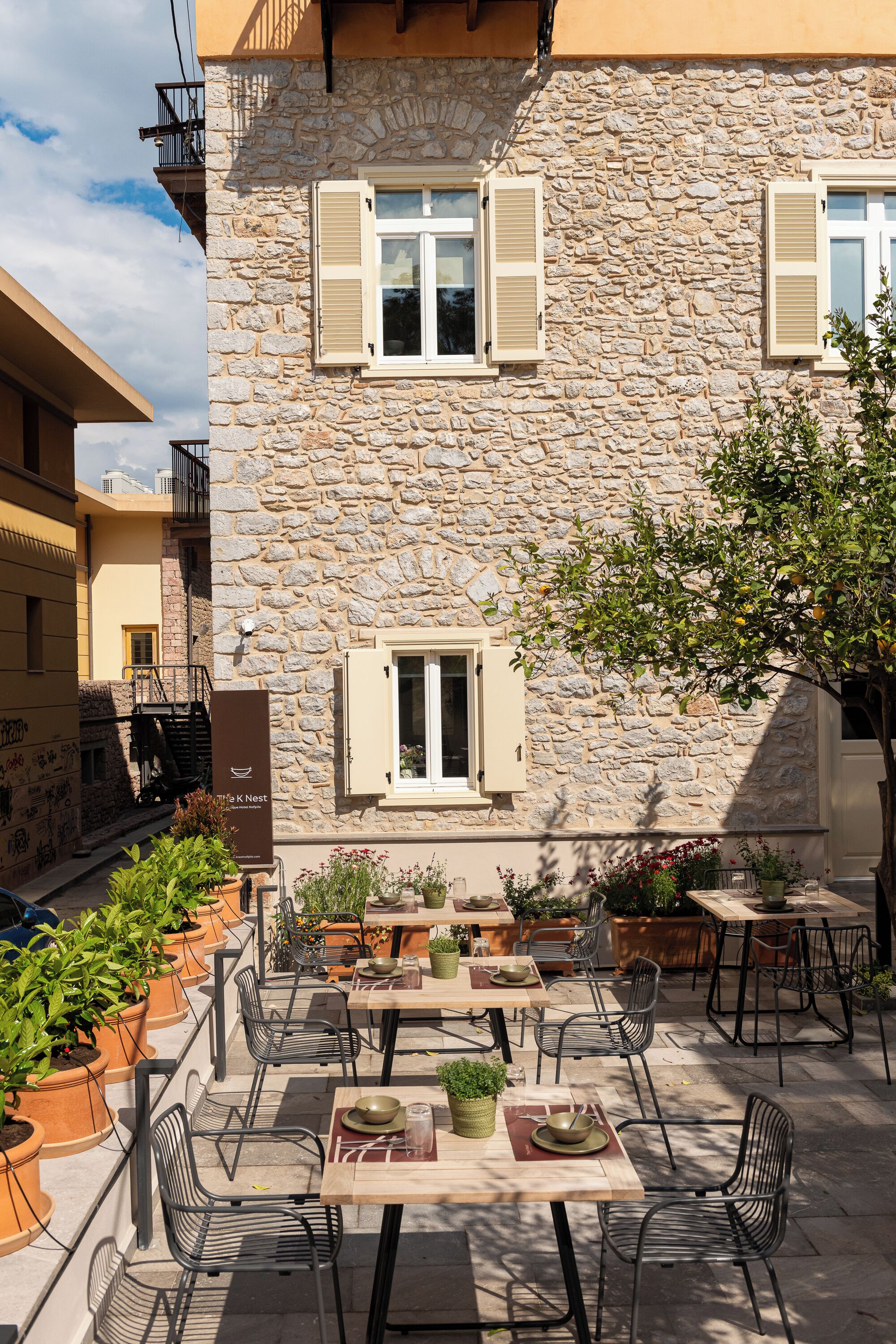 Un edificio de piedra con terraza, mobiliario exterior y macetas con plantas.