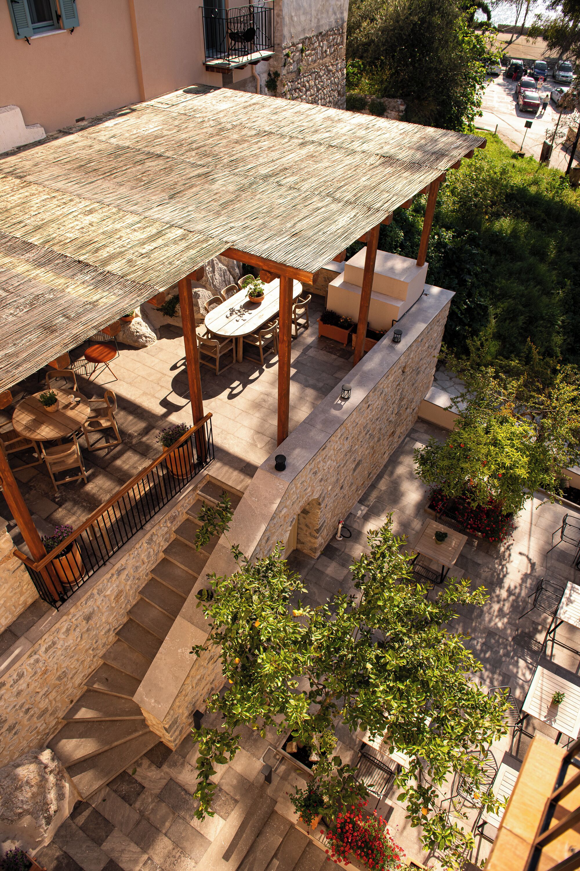Un patio exterior techado con suelo de piedra, muebles de madera y plantas en macetas.