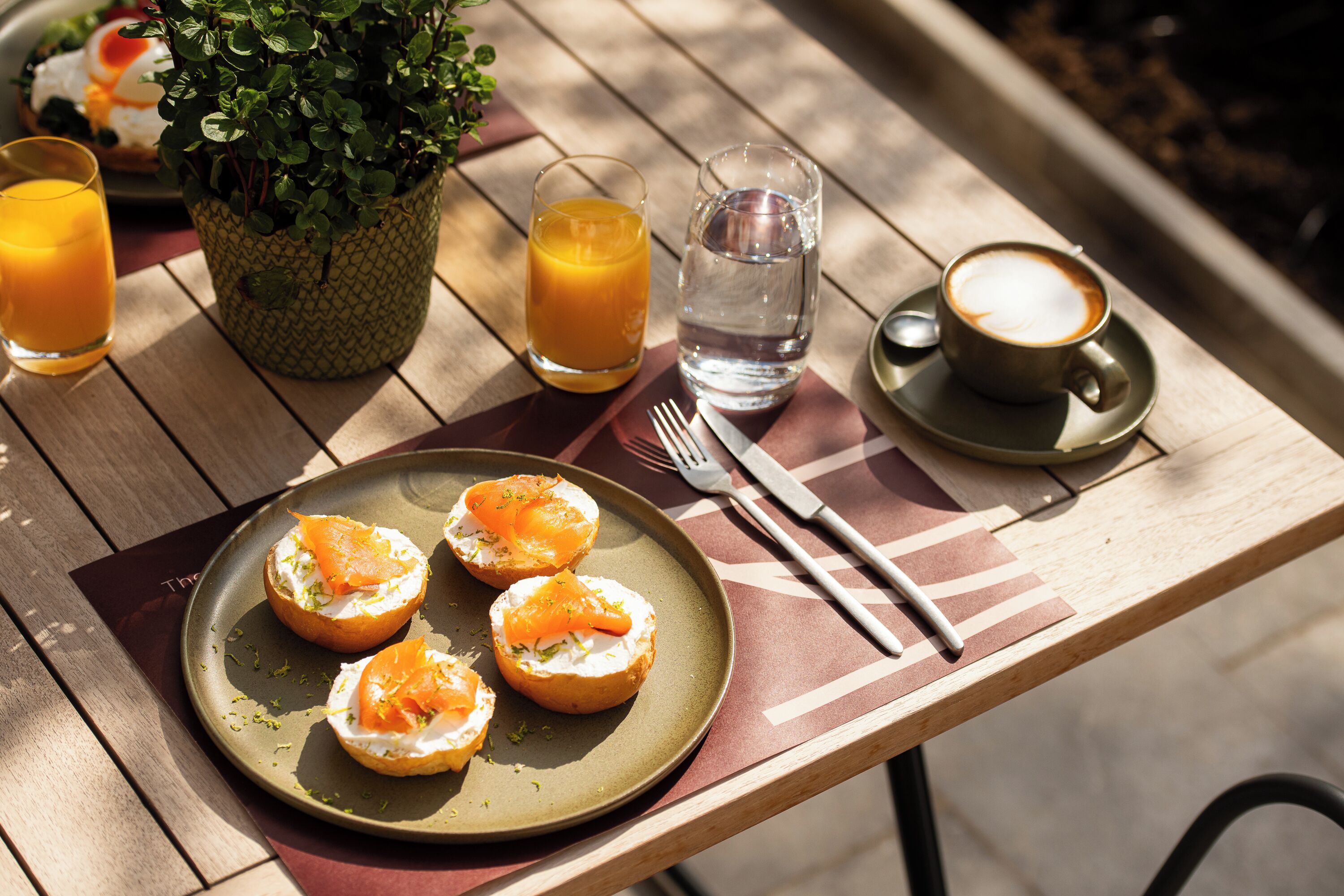 A wooden table with a plate of open-faced sandwiches, a glass of orange juice, a glass of water, and a cup of coffee.