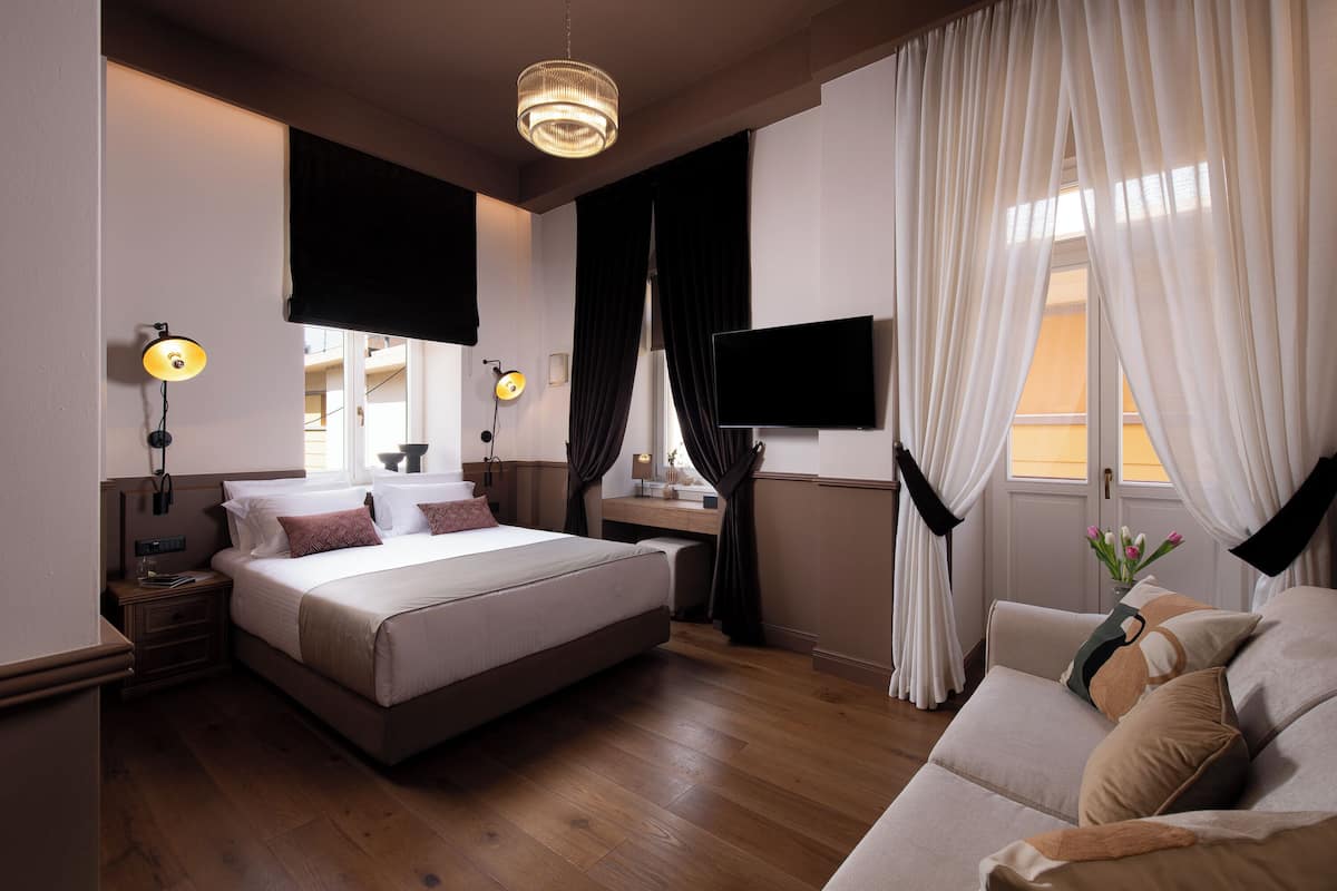 Ett modernt hotellrum med en stor säng, sängbord, ett skrivbord, en platt-TV och en soffa.