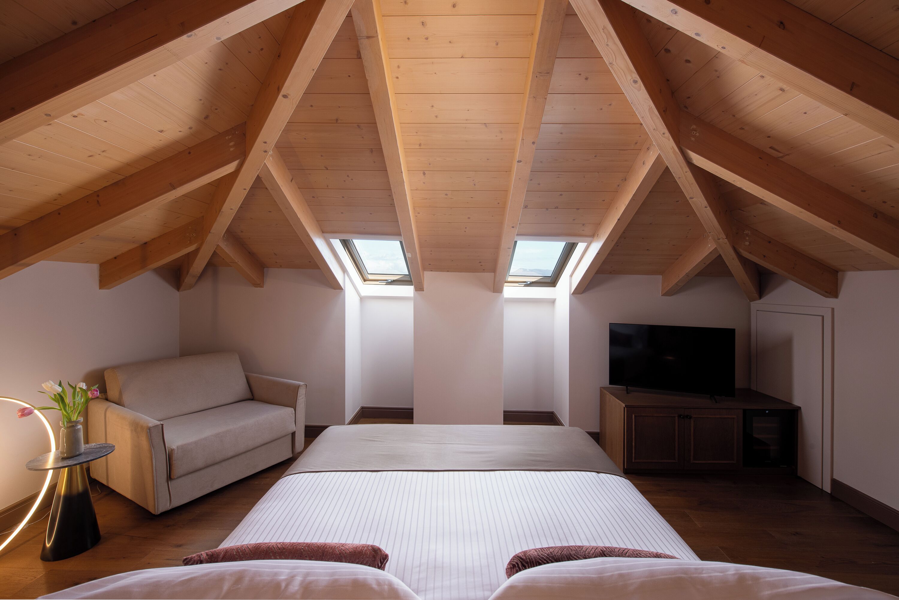 A bedroom with a large bed, a sofa, a television, and skylights.