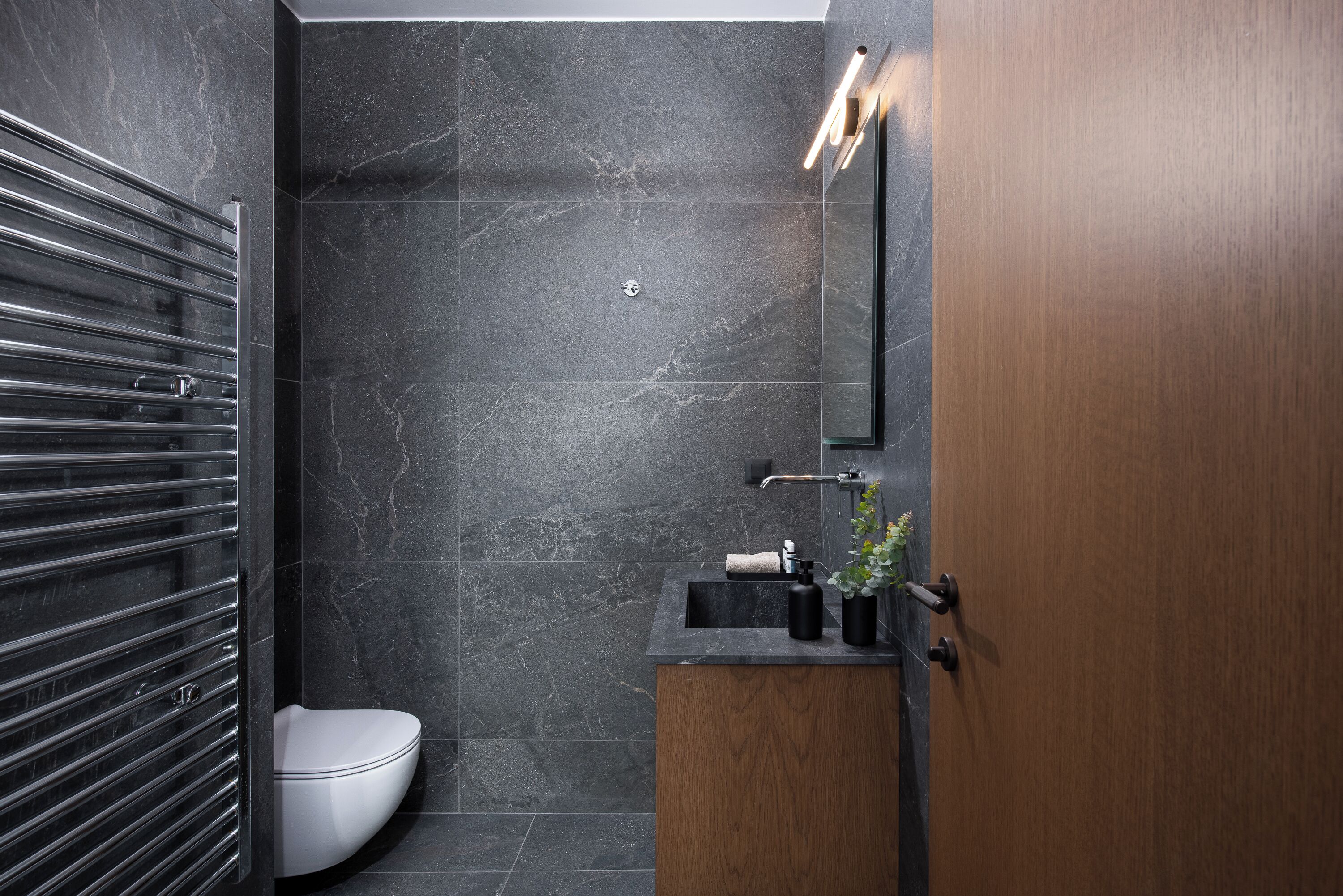 A modern bathroom with a toilet, a wooden vanity, and a mirror.